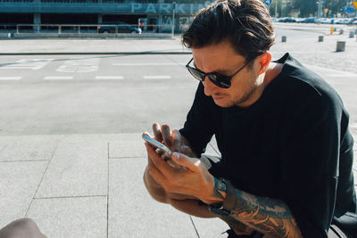 Man wearing sunglasses using smart phone on sidewalk