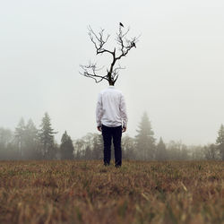 Rear view of man standing on field against bare tree