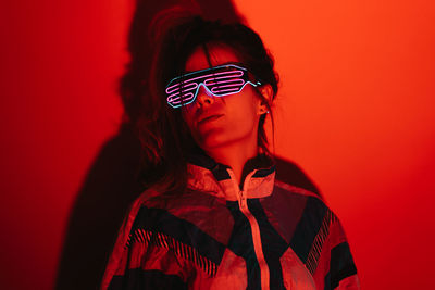 Young female in stylish sunglasses and old fashioned attire standing in studio with red light