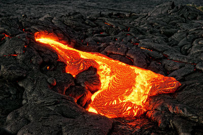 A lava flow emerges from a rock column and pours into a black volcanic landscape