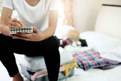 Midsection of woman writing in book while sitting on bed at home