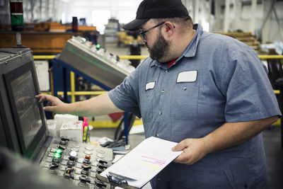 Overweight manual worker operating machinery at control panel in metal industry