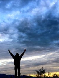 Rear view of silhouette man with arms outstretched against dramatic sky