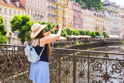 Woman photographing with umbrella standing on railing in city