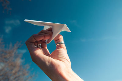 Low angle view of person holding hands against blue sky