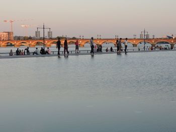 Group of people near water against clear sky during sunset