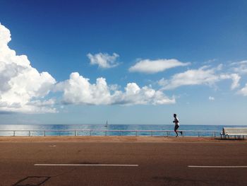 Man running on sidewalk by sea against sky