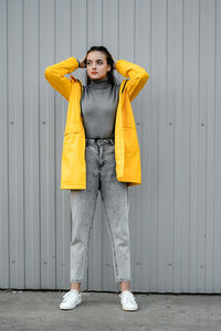 Girl in a yellow raincoat and gray jeans stands on a gray background. youth subculture