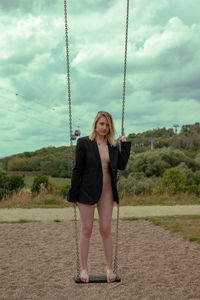 Full length portrait of woman standing on swing in playground