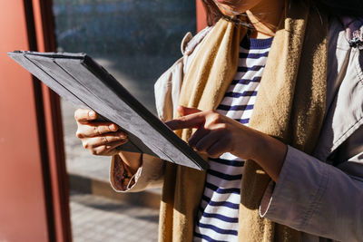 Cropped unrecognizable female standing against reflecting mirrored wall and browsing gadget on sidewalk in sunny day