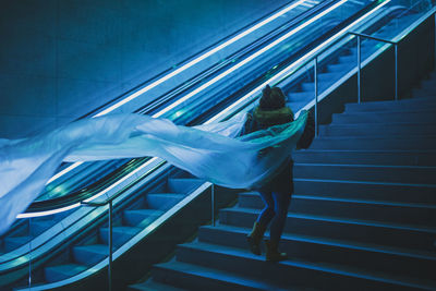 Rear view of young woman holding plastic on steps