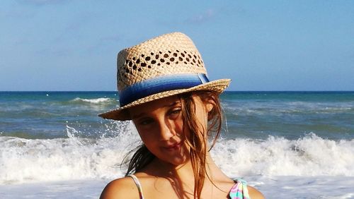 Portrait of smiling girl wearing sun hat standing at beach against clear sky