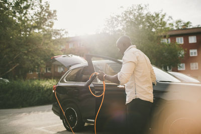 Mid adult man holding electric cable by car on driveway