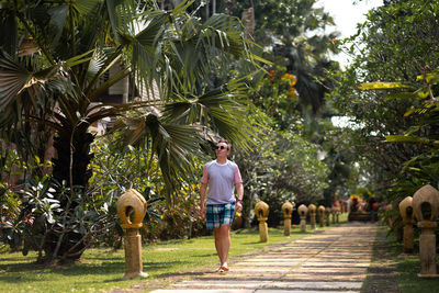 Man walking on footpath by palm trees