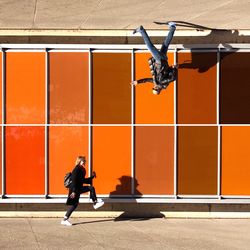 Full length of man paragliding against orange wall