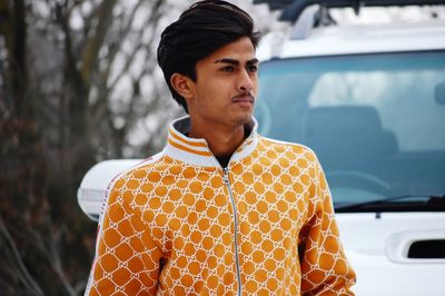 Young man looking away while standing by car