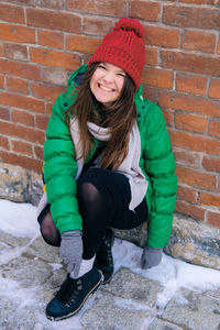 Portrait of smiling woman sitting against brick wall