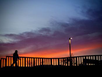 Silhouette man by railing against sky during sunset