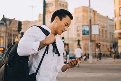 Side view of man using mobile phone while standing on street