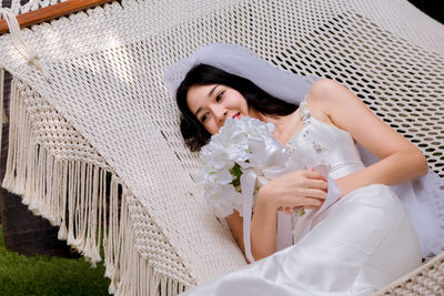 High angle view of bride holding bouquet relaxing on hammock outdoors