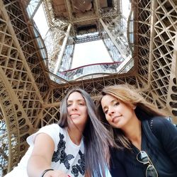 Low angle portrait of smiling friends standing below eiffel tower