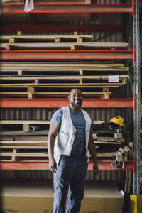 Portrait of smiling carpenter standing against pallet stack in warehouse