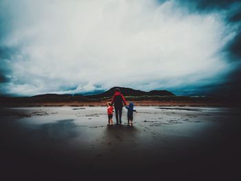 Rear view of men standing on beach against sky