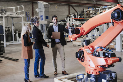 Businessman explaining colleagues over robotic arm at industry