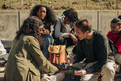 Smiling man applying nail polish on hand of woman while sitting by friends in park