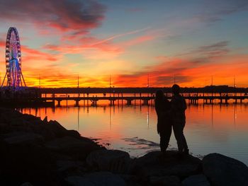 Silhouette people standing on rock by sea against sky during sunset