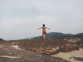 Rear view of man standing on rock against sky