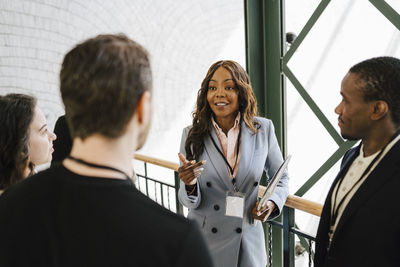 Businesswoman gesturing while discussing with male and female colleagues during networking event