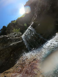 Low angle view of waterfall against sky on sunny day