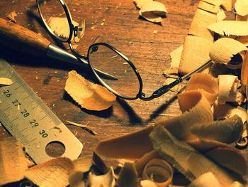 Close-up of eyeglasses with chisel and ruler by sawdust on table