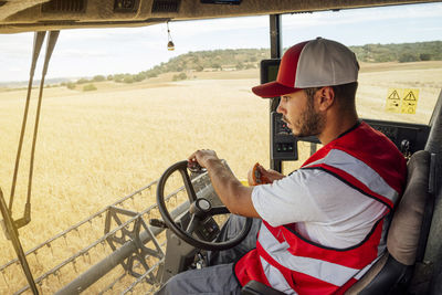 Side view of combine operator in uniform harvesting grain crops in agricultural field while working in rural area