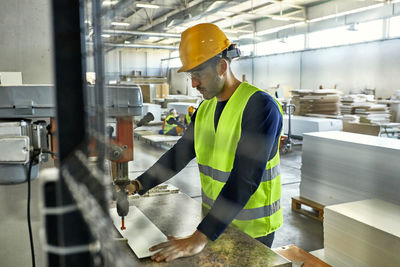 Worker operating drill in factory