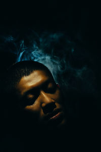 Close-up of young man with eyes closed against black background