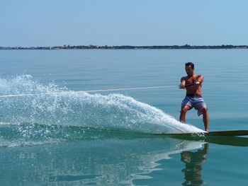 Full length of shirtless man wakeboarding in sea against clear sky