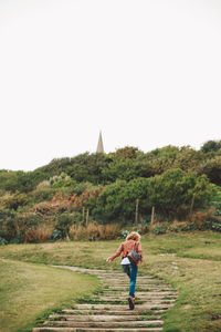 Woman walking on boardwalk towards forest against sky