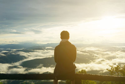 Rear view of man looking at mountain against sky during sunset