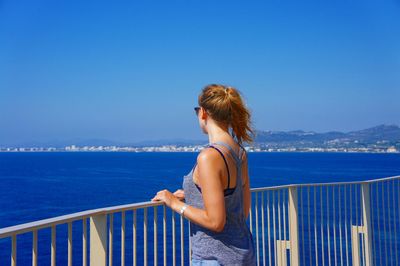 Young woman by railing looking at sea on sunny day