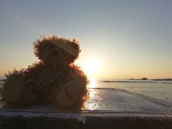 Close-up of stuffed toy on beach against sky during sunset