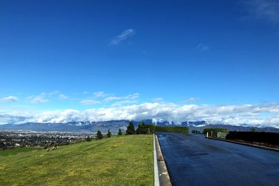 Road leading towards city against blue sky