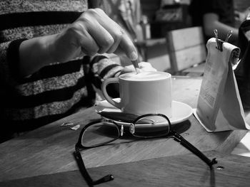 Midsection of person stirring coffee by eyeglasses on table