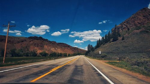 Empty road by mountains against blue sky