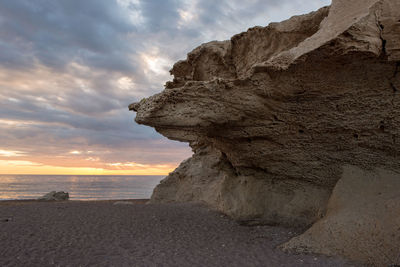 Rock formation on beach against sky during sunset
