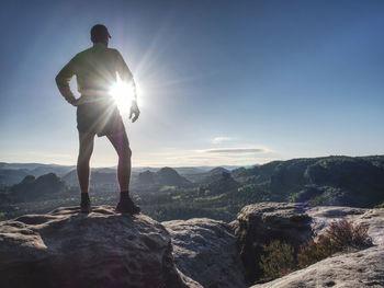 Rear view of man standing on rock against sky