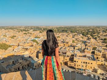 Rear view of woman looking at cityscape against sky