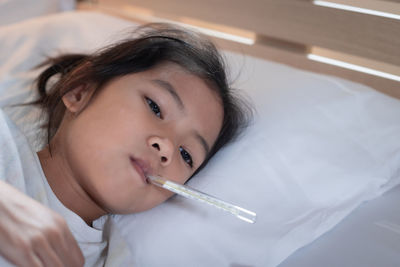 Cute girl with thermometer lying on bed at home