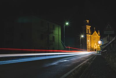 Light trails on street amidst illuminated buildings in city at night